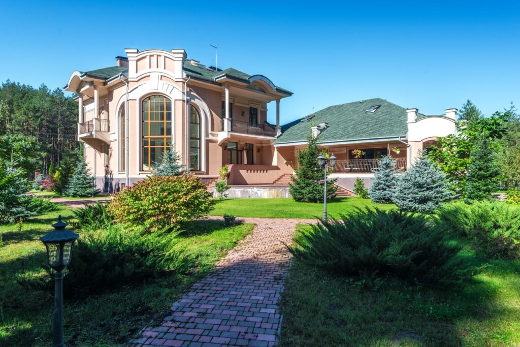 Beautiful mansion in sunny weather, surrounded by lush greenery and a clear blue sky.